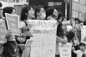 立ち上がる保護者。市の計画に反対し市役所前に立つ保護者たち＝３月８日、八尾市内