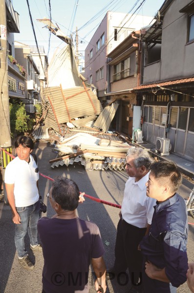  ビル屋上にあった雨よけのトタン屋根が暴風で吹き飛ばされて垂れ下がり、道路が通行不能に。現場で状況を聞く、たつみ参院議員、尾上やすお大阪市議、あだち雅之府議候補＝５日午後、大阪市西成区内