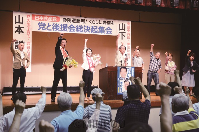 大阪二区地区委員会が参院選勝利に向けて開いた総決起集会で、参加者と共に決意を固め合う、山下よしき副委員長（舞台上左から２人目）、山本のりこ比例候補（同３人目）＝６月19日、大阪市平野区内 