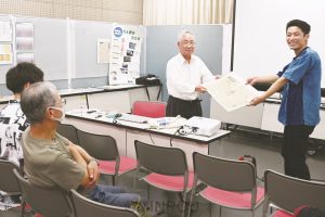 貴重な戦時資料を手渡す柏木さん（左）と青年＝23日、吹田市内